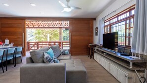 Amplia sala de estar con sofá, mesa de comedor con sillas, televisor y un ventanal con cortinas.