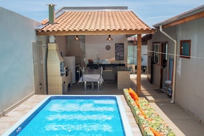 A poolside area with a tiled roof, a barbecue, a dining table, and a small kitchen area. - Casa c Piscina e Churrasqueira na Praia Maranduba (Ubatuba)