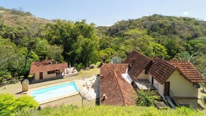 Una propiedad en una ladera con piscina, varias edificaciones con techos a dos aguas y abundante vegetación.