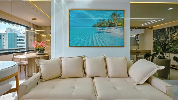 Een moderne woonkamer met een beige bank, een ronde eettafel en een groot schilderij van een strand.