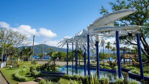 Une grande sculpture représentant le squelette d’une baleine, installée dans un parc avec une piscine et de la verdure.