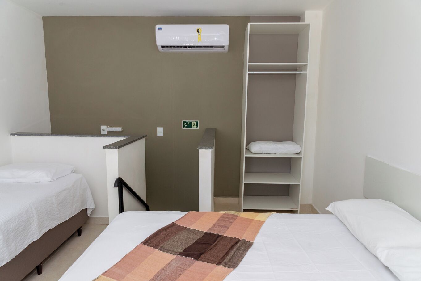 A hotel room with a bed, a bedside table, a wardrobe, and an air conditioning unit.