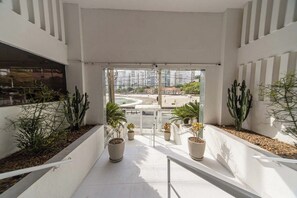 Ein modernes Interieur mit einer Glastür, die zu einem Außenbereich führt, mit Topfpflanzen und Blick auf eine Stadtlandschaft.
