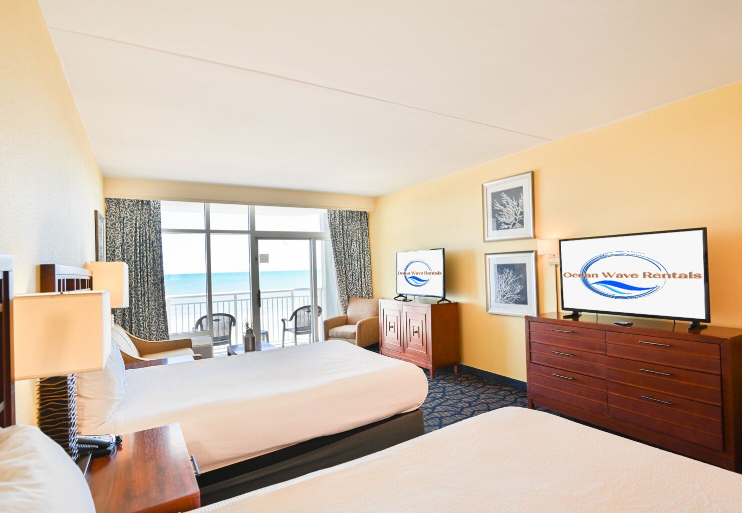 A hotel room with two beds, a TV, a desk, a chair, and a view of the ocean.