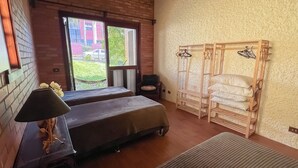 Ein Zimmer mit zwei Betten, einer Holzbank, einem Kleiderständer und Blick nach draußen.
