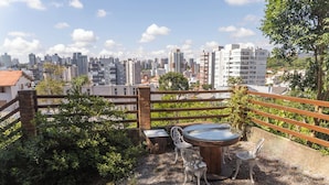 Eine Dachterrasse mit rundem Tisch und Stühlen, umgeben von einem Holzzaun und Grünpflanzen.