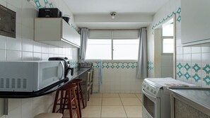 A compact kitchen with a microwave, stove, and bar stools. - Apto Pet Friendly com Garagem na Praia do Morro (Guarapari)