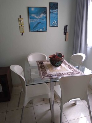 A dining area with a glass table, white chairs, and a decorative bowl. - Apto Pet Friendly com Garagem na Praia do Morro (Guarapari)