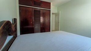 A bedroom with a bed, wooden wardrobe, and a door leading to another room. - Apto Pet Friendly com Garagem na Praia do Morro (Guarapari)