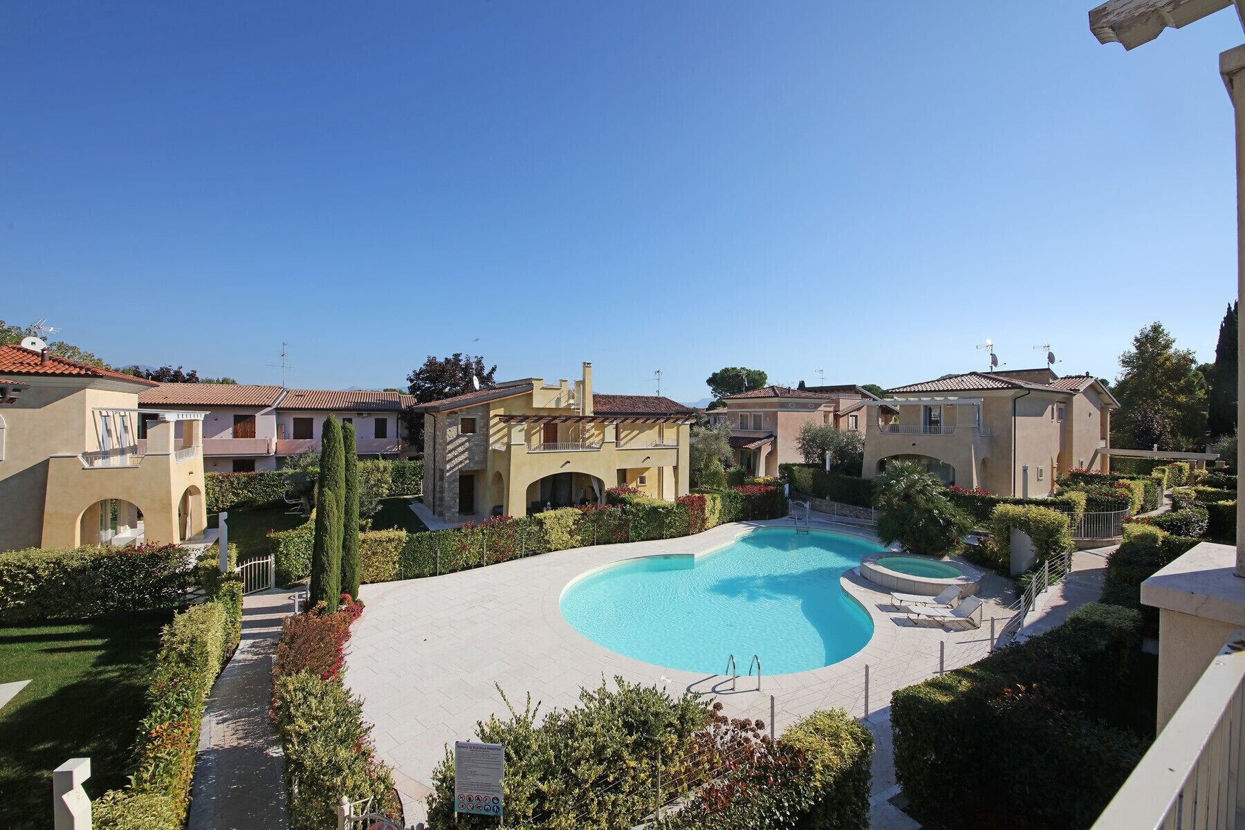 Un quartier résidentiel doté d’une piscine, entouré de jardins bien entretenus et de maisons à l’architecture méditerranéenne.