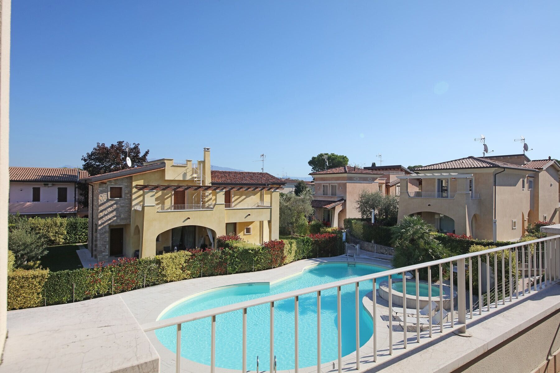A residential area with a swimming pool, houses with balconies, and a clear blue sky.