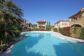 Ein Swimmingpool, umgeben von üppiger Vegetation und Gebäuden im mediterranen Stil.