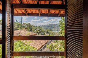 Blick durch ein hölzernes Fenster mit Ziegeldach auf ein Wohngebiet mit Häusern und Grünflächen.