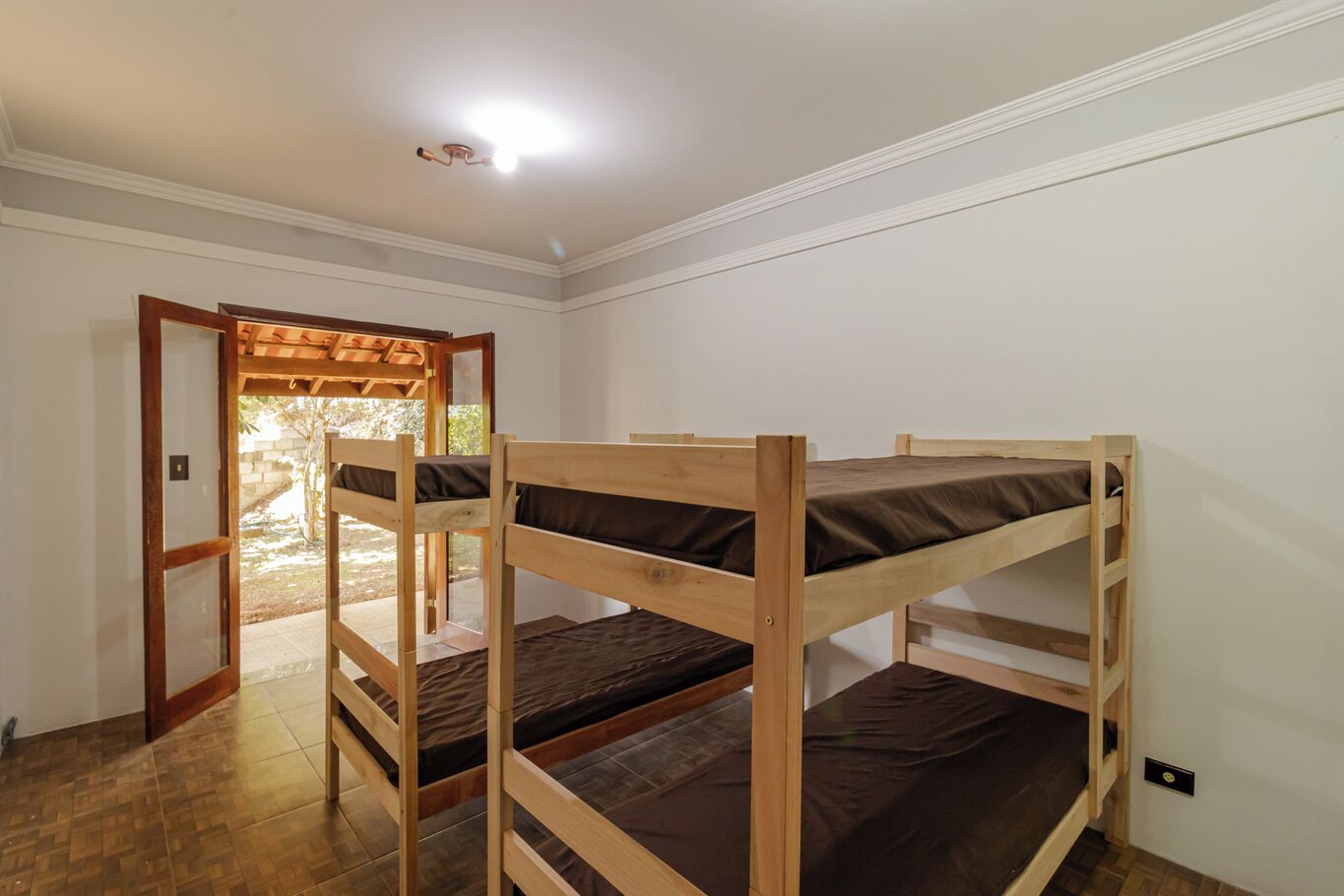 A room with three bunk beds, a wooden door leading outside, and a ceiling light.