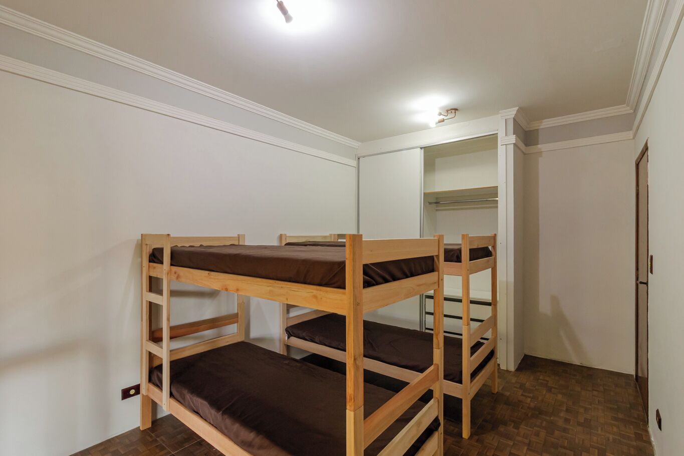 A bunk bed room with white walls, a wooden floor, and a closet in the background.
