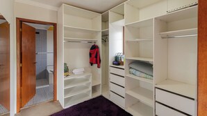 Ein begehbarer Kleiderschrank mit mehreren Regalen und Schubladen, einer Kleiderstange und einer Tür zu einem weiteren Raum.