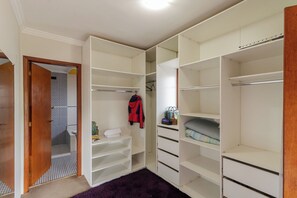 Ein begehbarer Kleiderschrank mit mehreren Regalen und Schubladen, einer Kleiderstange und einer Tür zu einem weiteren Raum.