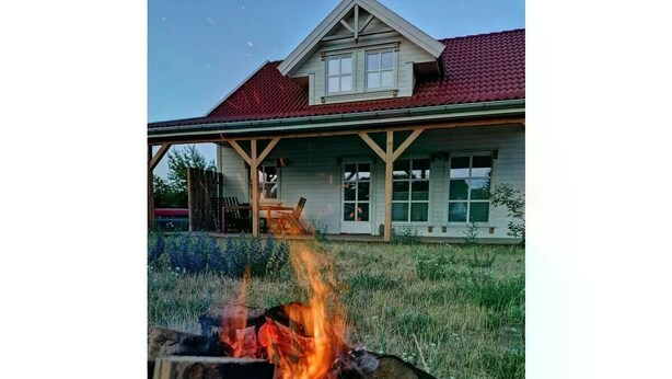 A fire pit with flames, a wooden deck, and a house with a red roof in the background. - Vacation cottage Hus Hygge Warin (Warin)