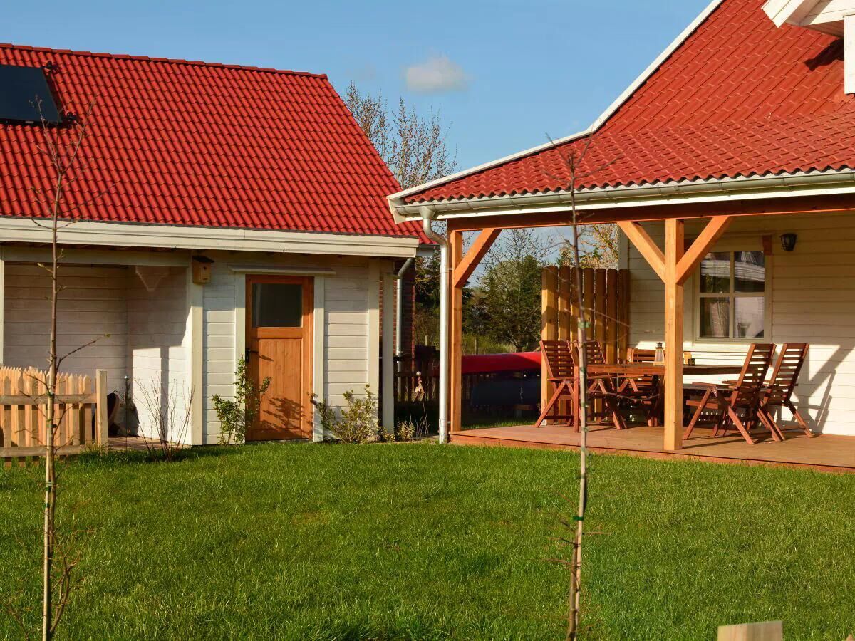 A two-story house with a red-tiled roof, a covered patio with wooden furniture, and a well-maintained lawn.