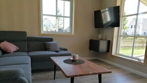 A living room with a grey sofa, a wooden coffee table, and a TV mounted on the wall. - Vacation cottage Hus Hygge Warin (Warin)