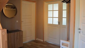 A room with a wooden floor, two white doors, a coat rack, and a small white chair. - Vacation cottage Hus Hygge Warin (Warin)