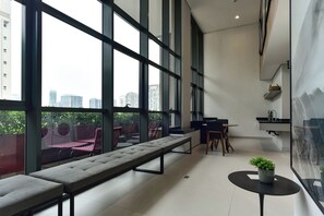 Ein modernes Interieur mit großen Fenstern, einer Sitzecke mit Bänken, einem Esstisch und einem kleinen runden Tisch mit einer Pflanze.