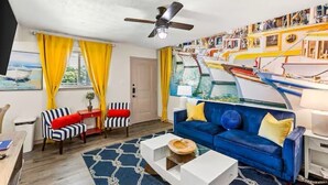 A living room with a blue sofa, striped chairs, a ceiling fan, and a wall with nautical-themed decorations. - The Tides of Galveston (Galveston)
