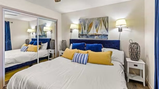A bedroom with a large bed, two bedside tables, a mirror, and a painting on the wall. - The Tides of Galveston (Galveston)