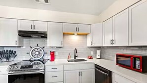 A modern kitchen with white cabinets, a built-in oven, a microwave, and a sink. - The Tides of Galveston (Galveston)