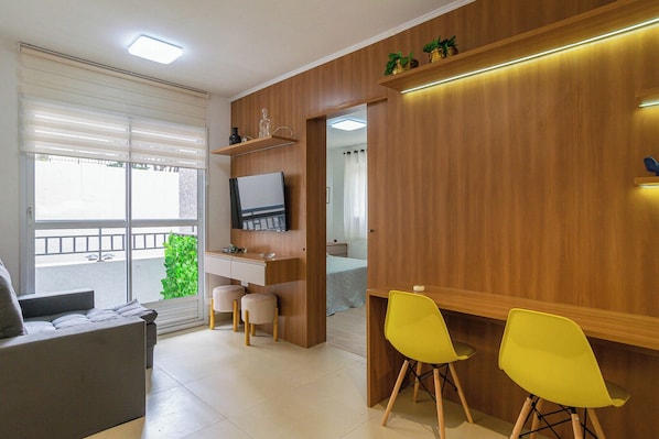 A modern living room with a sofa, a desk, two yellow chairs, and a TV mounted on the wall.