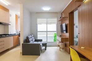 A compact living space with a kitchenette, a sofa, a dining table, and a TV mounted on the wall.