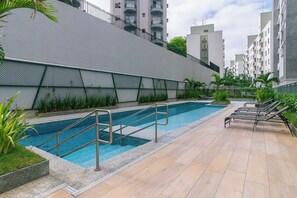 A swimming pool with steps and lounge chairs, surrounded by a fence and greenery.
