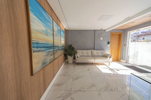Ein modernes Interieur mit einem großen Gemälde einer Strandansicht, einem beigen Sofa und einer Topfpflanze.
