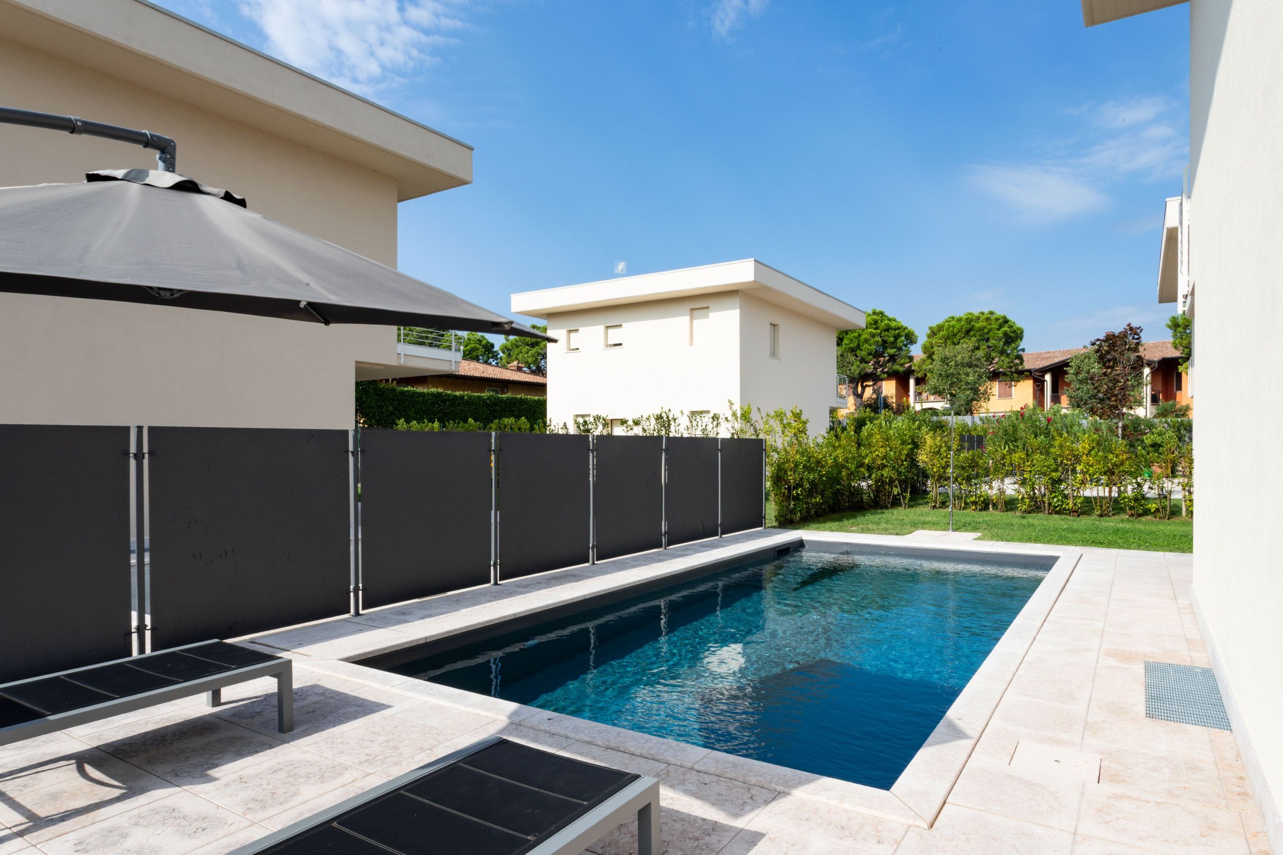 A swimming pool with a sun umbrella, a pergola, and a view of neighboring houses.