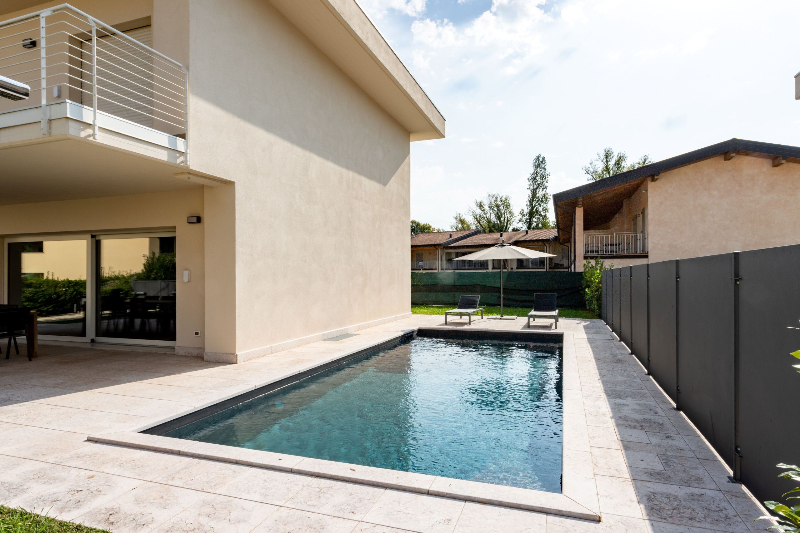 A swimming pool with a tiled deck, a covered patio area, and a view of a residential building in the background.