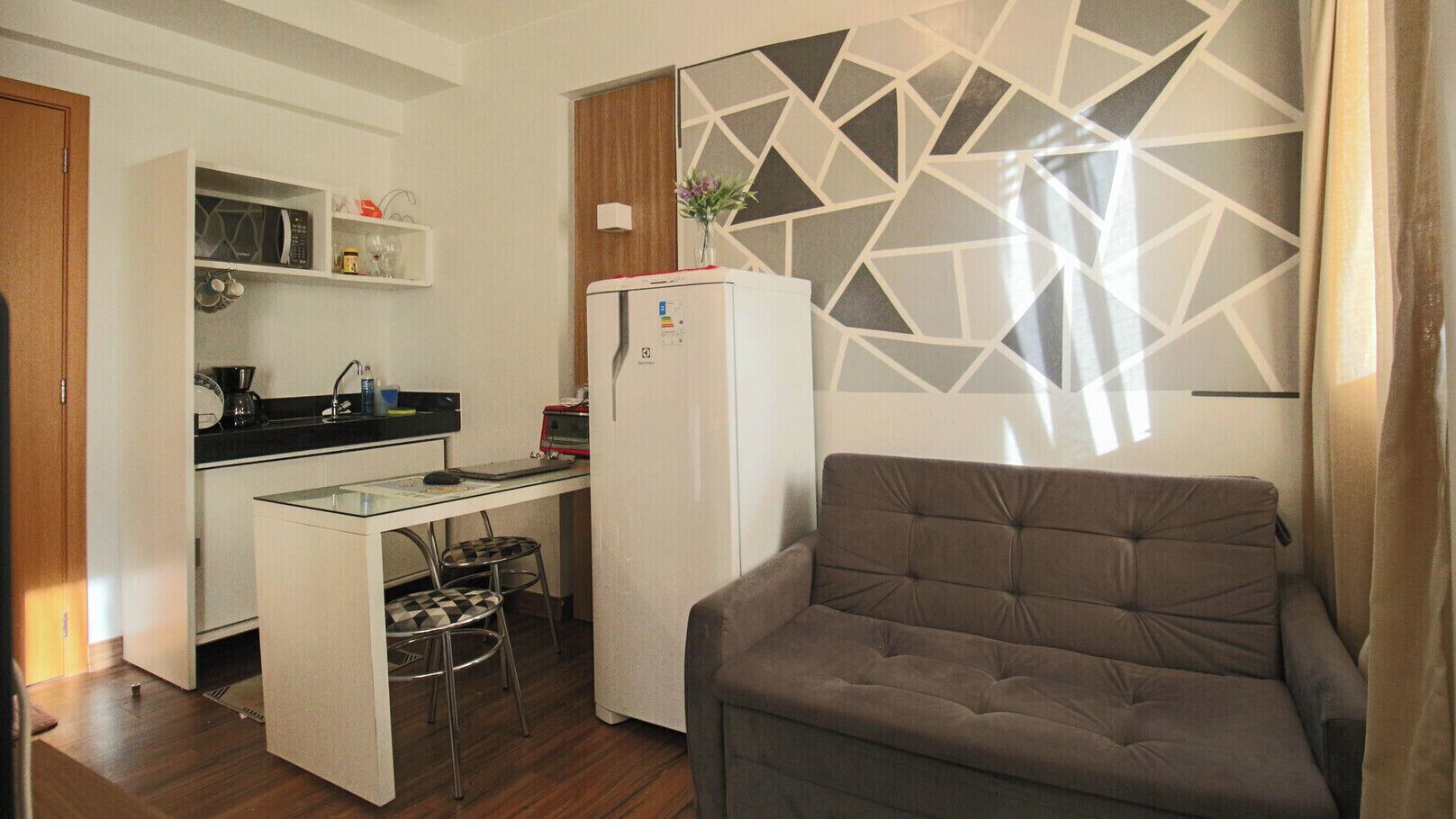 A compact kitchen with a refrigerator, microwave, and a small dining area with stools.