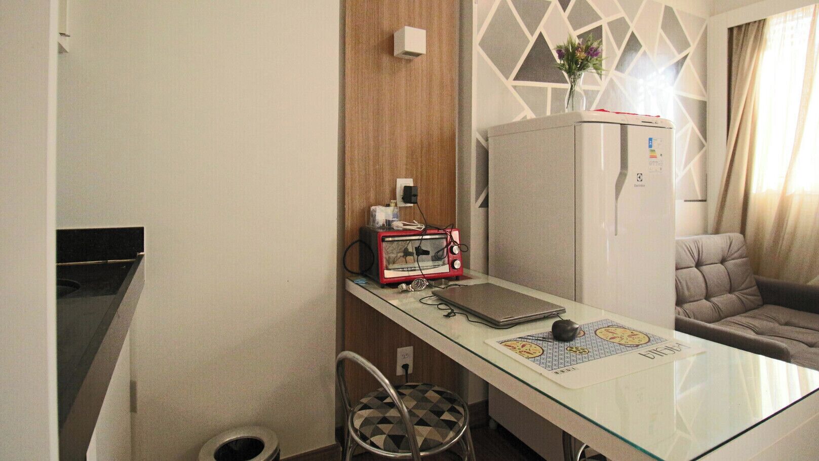 A compact kitchen with a glass-top table, a red retro toaster, and a refrigerator.