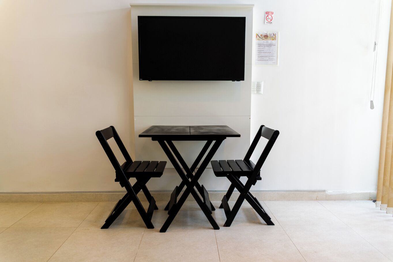 Una habitación pequeña con un televisor negro montado en la pared, una mesa negra y dos sillas negras.