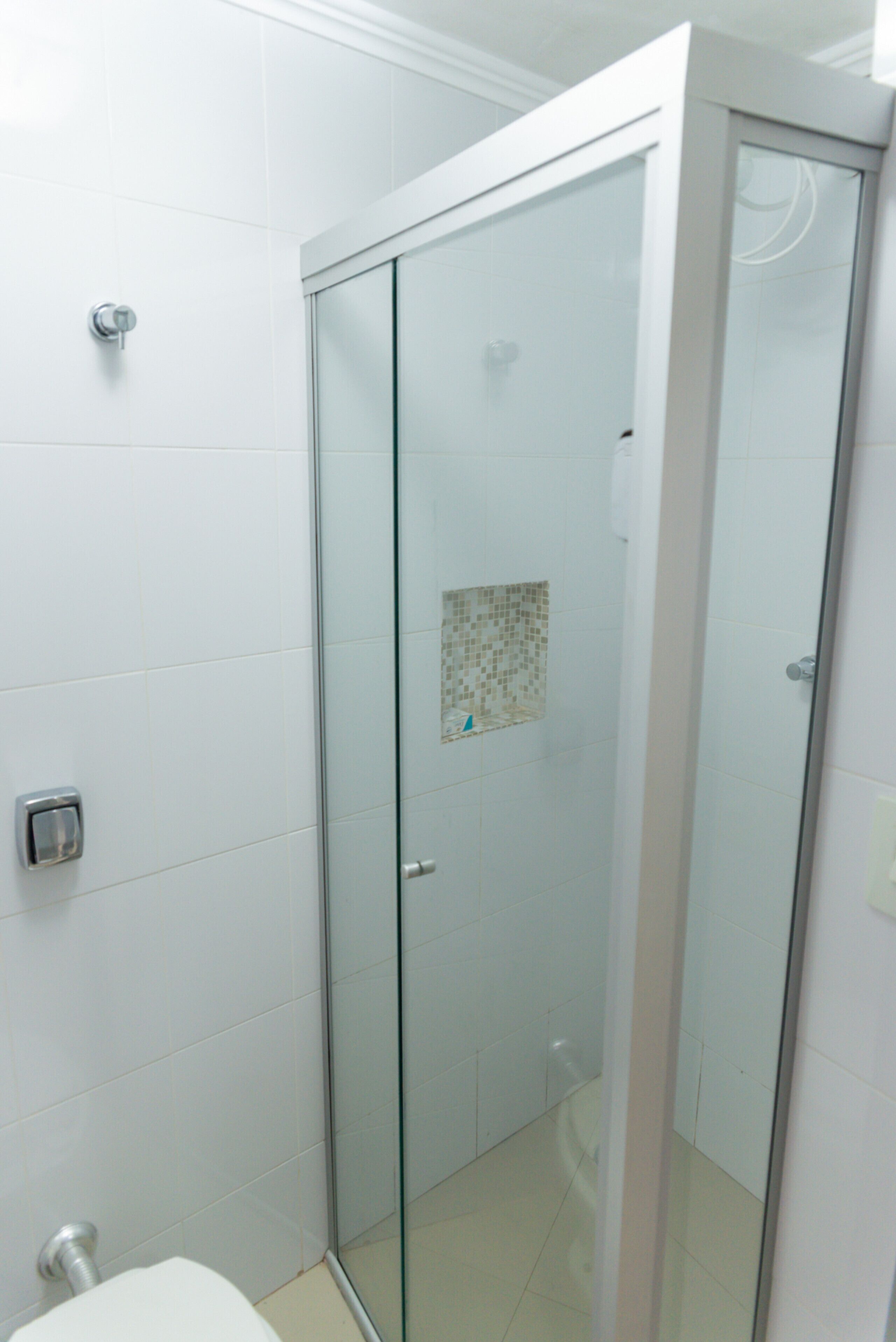 A bathroom with a glass-enclosed shower, white tiled walls, and a visible toilet.