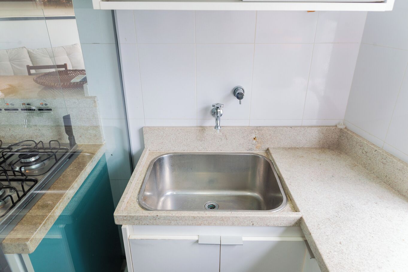 A kitchen with a stainless steel sink, a gas stove, and white tiled walls.
