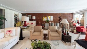A spacious living room with a brick wall, a dining area with striped chairs, and a red sofa. - Casa com Piscina, Churrasqueira, Jogos e Lareira (Petropolis)