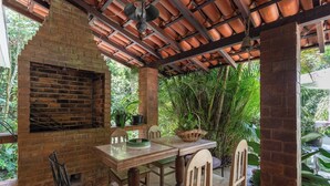 An outdoor patio with a brick fireplace, wooden table, and chairs. - Casa com Piscina, Churrasqueira, Jogos e Lareira (Petropolis)