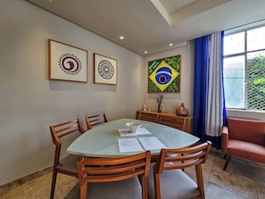 Ein Essbereich mit einem runden Glastisch, Holzstühlen, gerahmten Kunstwerken an der Wand und einer brasilianischen Flaggen-Dekoration.