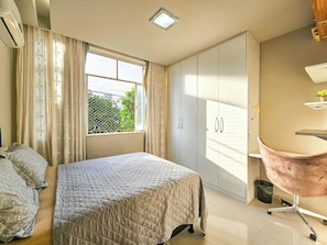 Ein Schlafzimmer mit Bett, Kleiderschrank, Schreibtisch, Stuhl und einem Fenster mit Vorhängen.