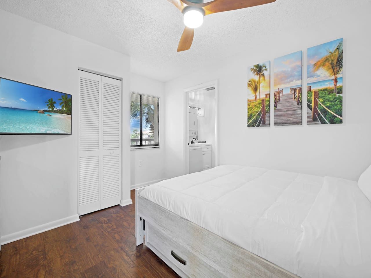 A bedroom with a bed, a ceiling fan, a wardrobe, a window, and wall art.