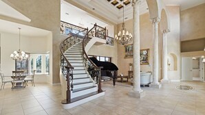 Ein geräumiges Foyer mit einer imposanten Treppe, einem Klavier und einer Chandelier.