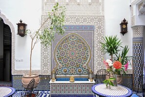 Een traditioneel Marokkaans interieur met ingewikkeld tegeltjeswerk, een potplant en een tafel met een bloevas.