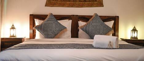 A bed with a wooden headboard, two patterned pillows, a white blanket, and a towel.