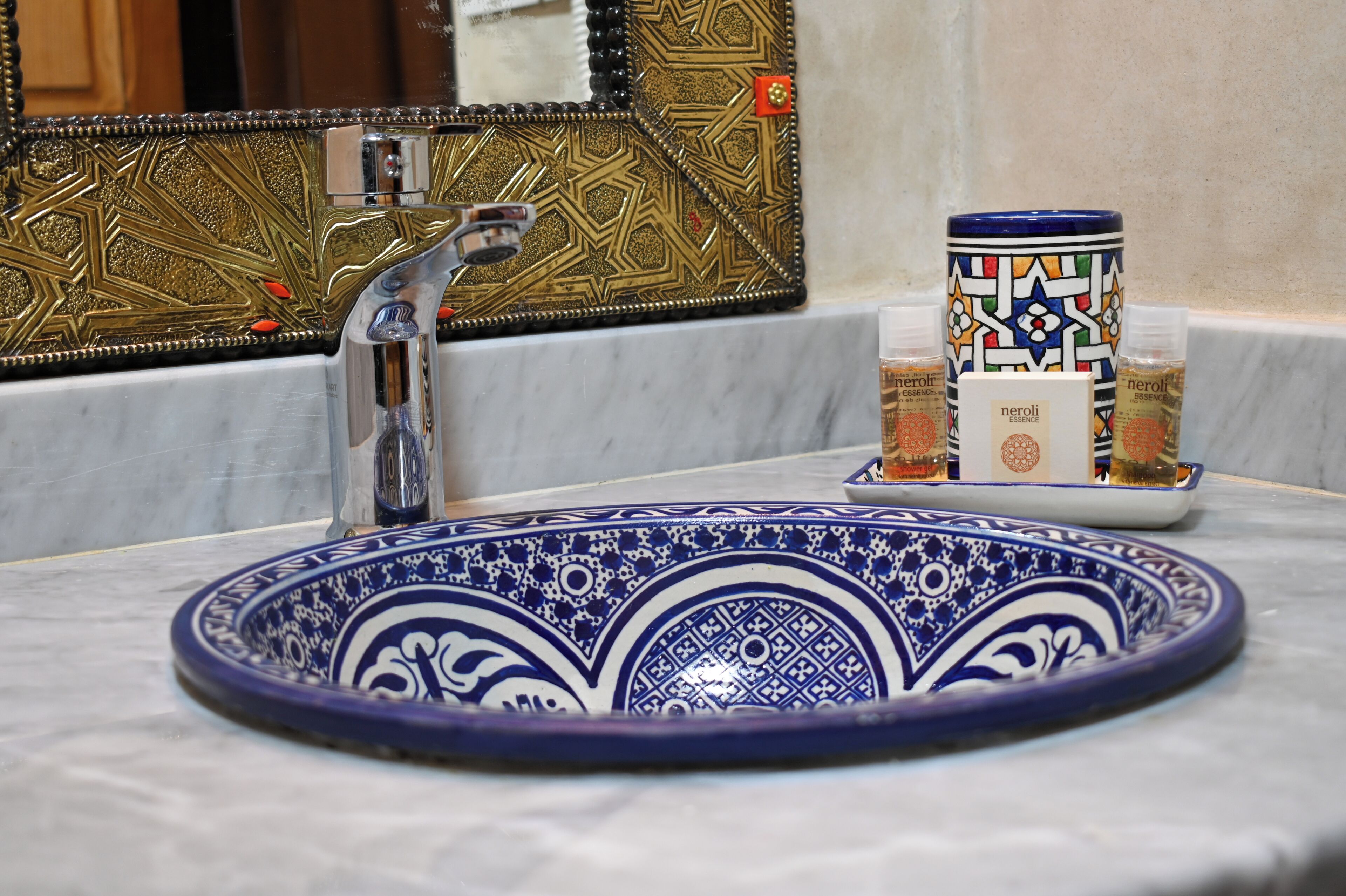 Un lavamanos de baño con un lavabo estampado en azul y blanco, un grifo moderno y un espejo decorativo de diseño geométrico.