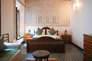 A bedroom with a wooden bed, a small round table, a chair, and a dresser.